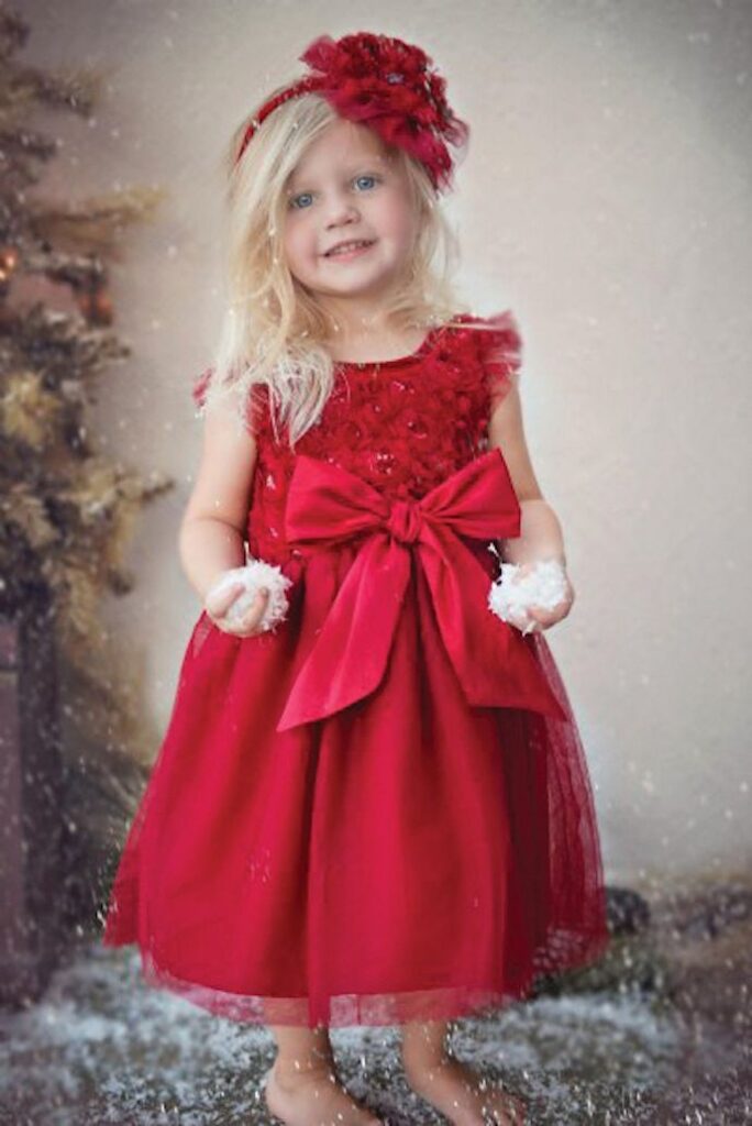 Little girl in red bow dress with hair fascinator holding faux snow flakes