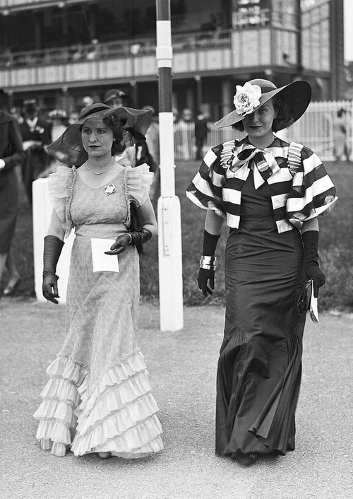 2 women in long gowns gloves and hats at the races circa 1930's