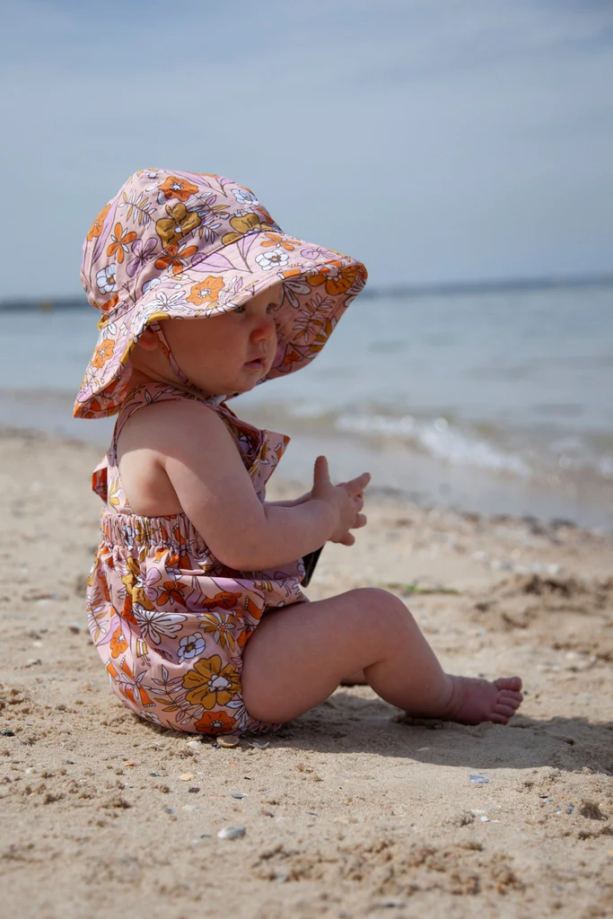 infant girl sitting on the beach in a playsuit and matching sun hat