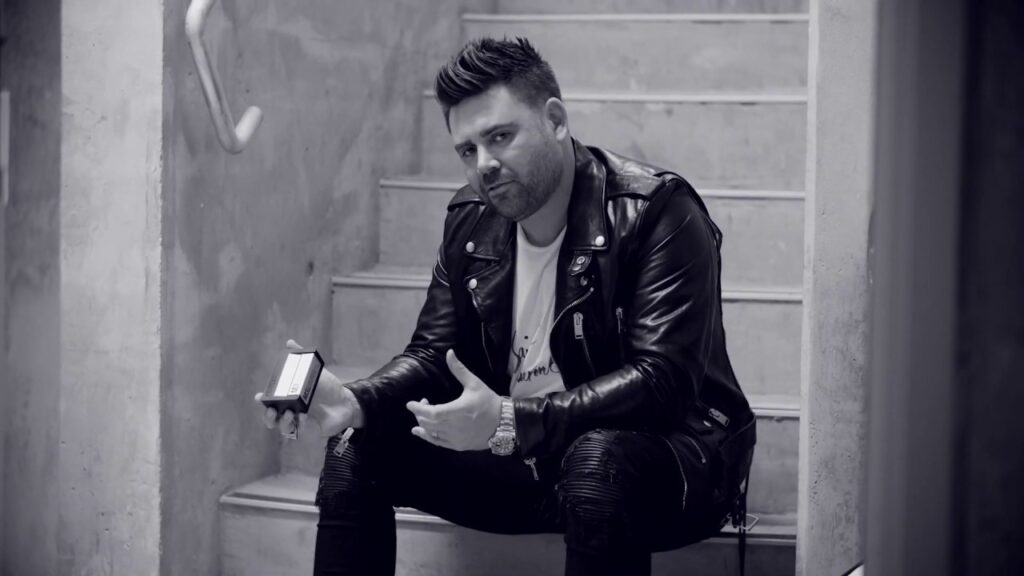 Black and white image of a man sitting on a set of stairs in a black leather jacket and white T.shirt