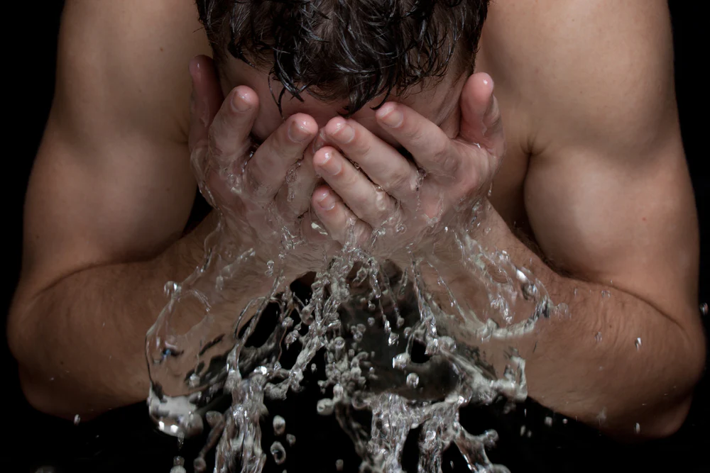 man without shirt splashing his face with water