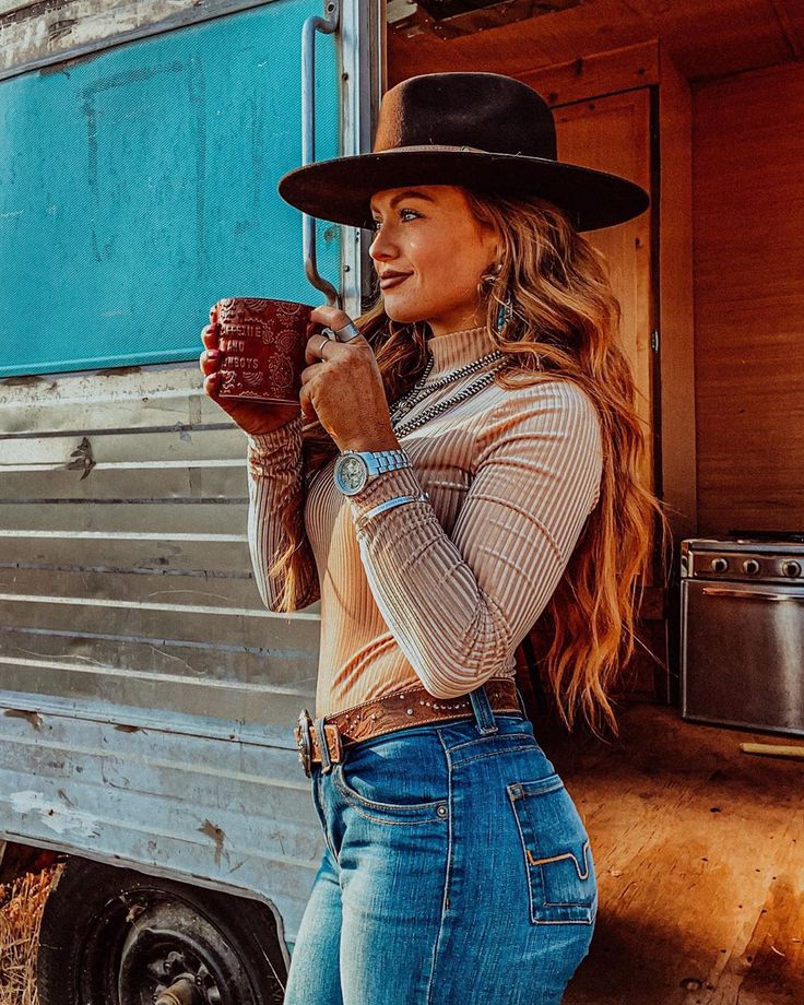 Cowgirl holding a cuppa wearing cowboy hat jeans and a light sweater