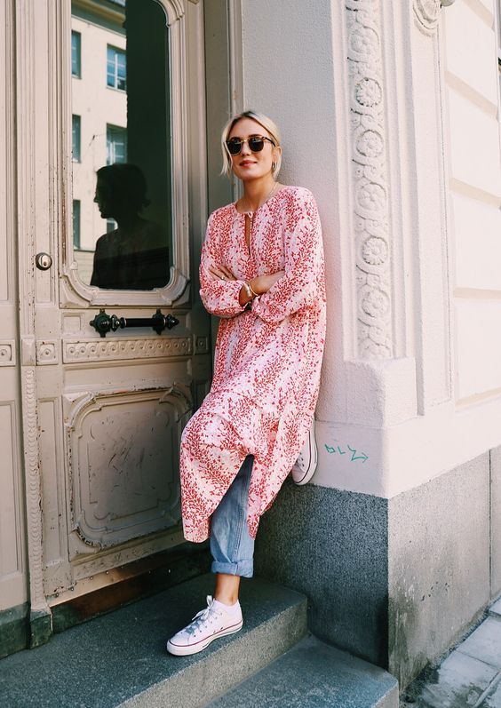 woman leaning on a building doorway wearing a long kaftan over jeans and sneakers