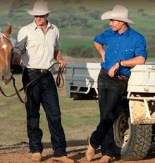 2 cowboys near a ute wearing black jeans hats and neutral toned shirts