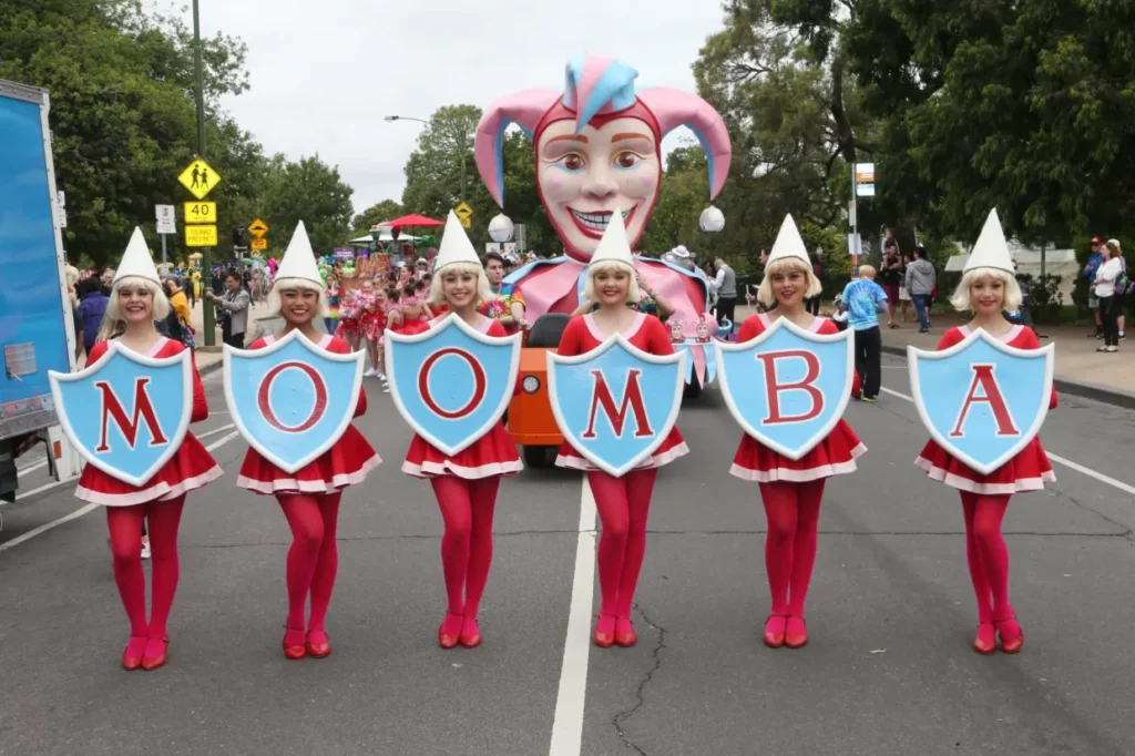 girls in tight red costumes holding up a vintage moomba sign in front of the joker. 