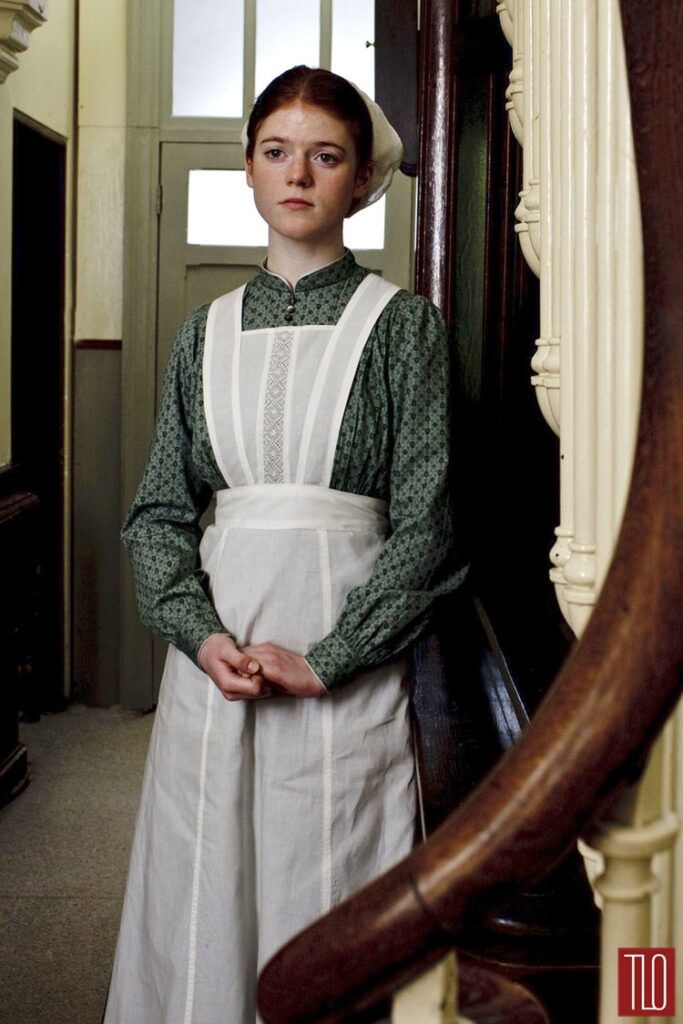 House maid in green toned dress with long sleeves and long apron