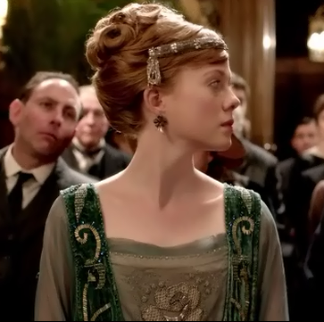 A socialite with red hair and an upswept hair style with diamond and emerald head piece