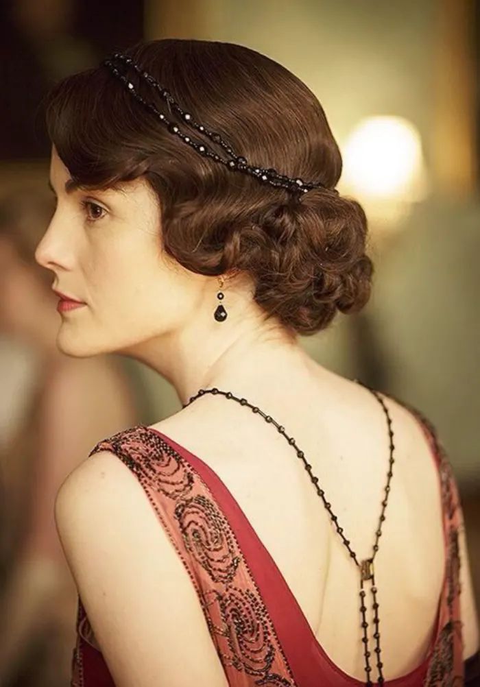 Lady Mary with a fingerwave hair style pinned in a bun and jewelry sweeping down her back and across her head