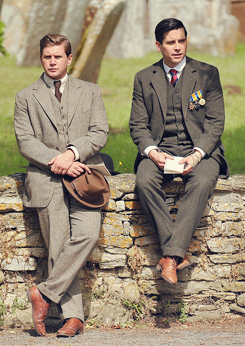 Two cast members relaxing on a fence in tweed 3 piece suits and brown shoes with ties
